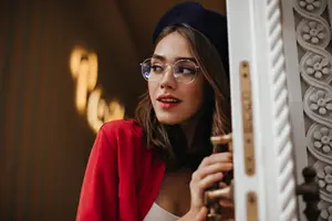 A woman with glasses, a hat, and a red jacket is opening a door.