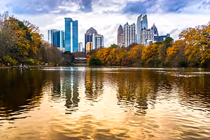 A city skyline with high-rise buildings, reflected on the water, surrounded by trees and a cloudy sky