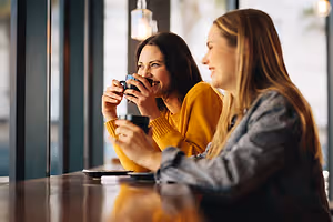 Two women sitting at a table in a restaurant, drinking coffee and smiling.