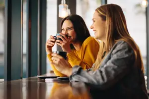 Two women sitting at a table in a restaurant, drinking coffee and smiling.