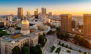 A golden domed building stands tall amidst the Stockbridge cityscape with high-rise buildings, green trees, and a clear blue sky with a setting sun in the background.