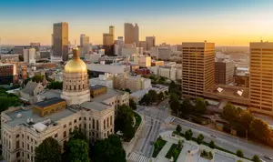 A golden domed building stands tall amidst the Stockbridge cityscape with high-rise buildings, green trees, and a clear blue sky with a setting sun in the background.