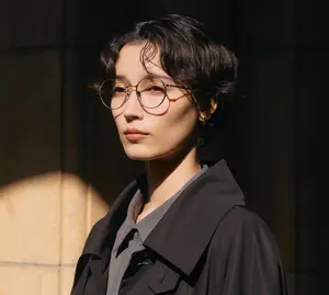 Asian woman with short hair wearing glasses and a black coat posing in front of a building