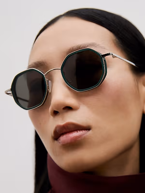 A woman wearing a pair of hexagonal sunglasses with green frames and silver accents