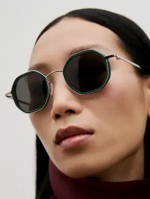 A woman wearing a pair of hexagonal sunglasses with green frames and silver accents