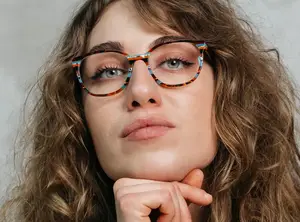 A woman with curly brown hair wearing round glasses with multicolored frames