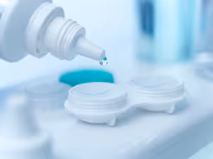 A close-up image of a person using eye drops in front of a blurry background