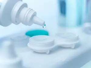 A close-up image of a person using eye drops in front of a blurry background