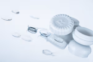 A close-up of a white contact lens container with a small white lens on top of a white surface.