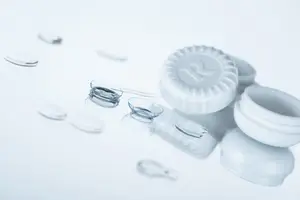 A close-up of a white contact lens container with a small white lens on top of a white surface.