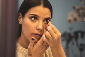 Woman applying contact lenses to her eyes in front of a mirror