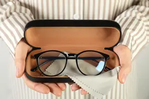 A pair of black-framed glasses in a black case with a white cloth inside.