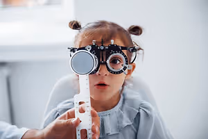 A young girl wearing glasses and looking up at a doctor holding a measuring stick