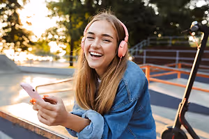 Girl with headphones listens to music on her phone at the skate park.