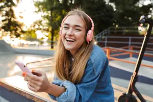 Girl with headphones listens to music on her phone at the skate park.