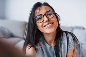 A smiling woman with glasses sitting on a couch