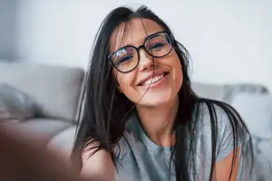 A smiling woman with glasses sitting on a couch