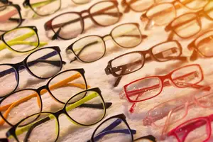 A collection of multicolored glasses with different frames and lenses displayed on a white cloth.