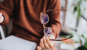 Person holding a pair of brown-framed glasses with a brown lens.