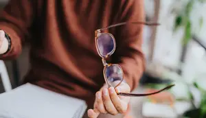 Person holding a pair of brown-framed glasses with a brown lens.