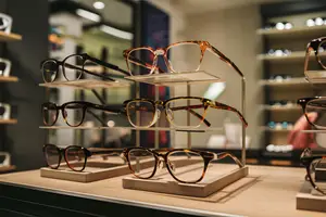 A display of various glasses in a retail shop, featuring three sets of glasses with wooden stands on a wooden shelf