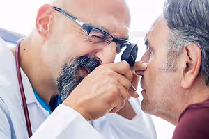 A doctor examining an older man's ear with an otoscope