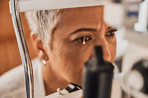 A person wearing glasses and looking through a microscope in a laboratory setting