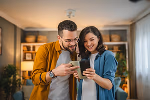 A man and a woman smiling while looking at a cell phone