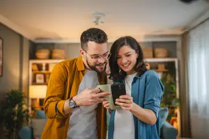 A man and a woman smiling while looking at a cell phone