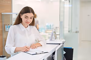 A woman in a white blouse writing on a clipboard at a reception desk