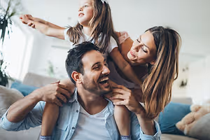 A family of three smiling at the camera in a living room