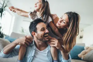 A family of three smiling at the camera in a living room