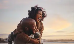 A man with a bald head carrying a woman on his shoulder and smiling while she laughs