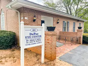A brick building with a white signboard that reads DePoe Eye Center and a phone number 770-228-1345