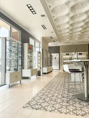 An interior of an optical shop with glass display cabinets and a table with chairs in front of a glass wall.