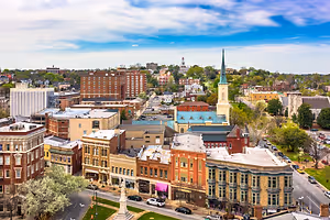 Aerial view of a city with multiple buildings, a statue, and cars driving on the road under a blue sky with white clouds