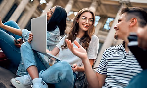 Three people sitting on steps with one holding a laptop and the other two smiling at the camera