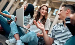 Three people sitting on steps with one holding a laptop and the other two smiling at the camera