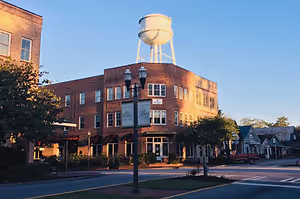 A city street with a red truck parked on the side, a water tower on a brick building, and a streetlight with a sign on it.