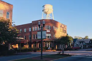 A city street with a red truck parked on the side, a water tower on a brick building, and a streetlight with a sign on it.