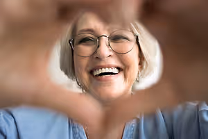 Woman wearing glasses smiling and making a peace sign with her fingers