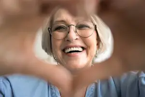 Woman wearing glasses smiling and making a peace sign with her fingers