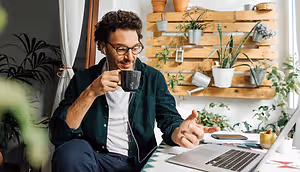 Man sitting on a chair and smiling while holding a cup and working on a laptop