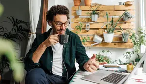 Man sitting on a chair and smiling while holding a cup and working on a laptop