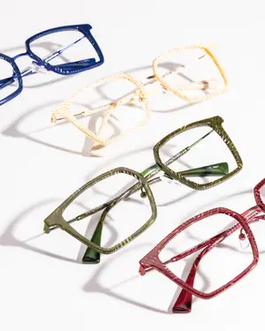 Five pairs of eyeglasses in blue, white, green, and red colors are displayed on a white surface, showcasing various frame styles and colors.