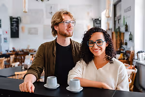 A man and woman standing behind a bar counter with cups on it