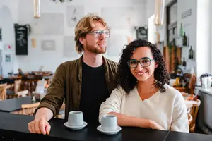 A man and woman standing behind a bar counter with cups on it