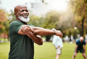 An older man stretching his arm in a park