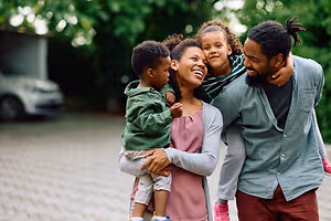 A happy family of three adults and two children are standing on a brick path, smiling and posing for a picture