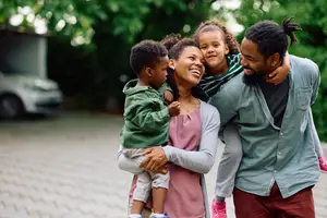 A happy family of three adults and two children are standing on a brick path, smiling and posing for a picture